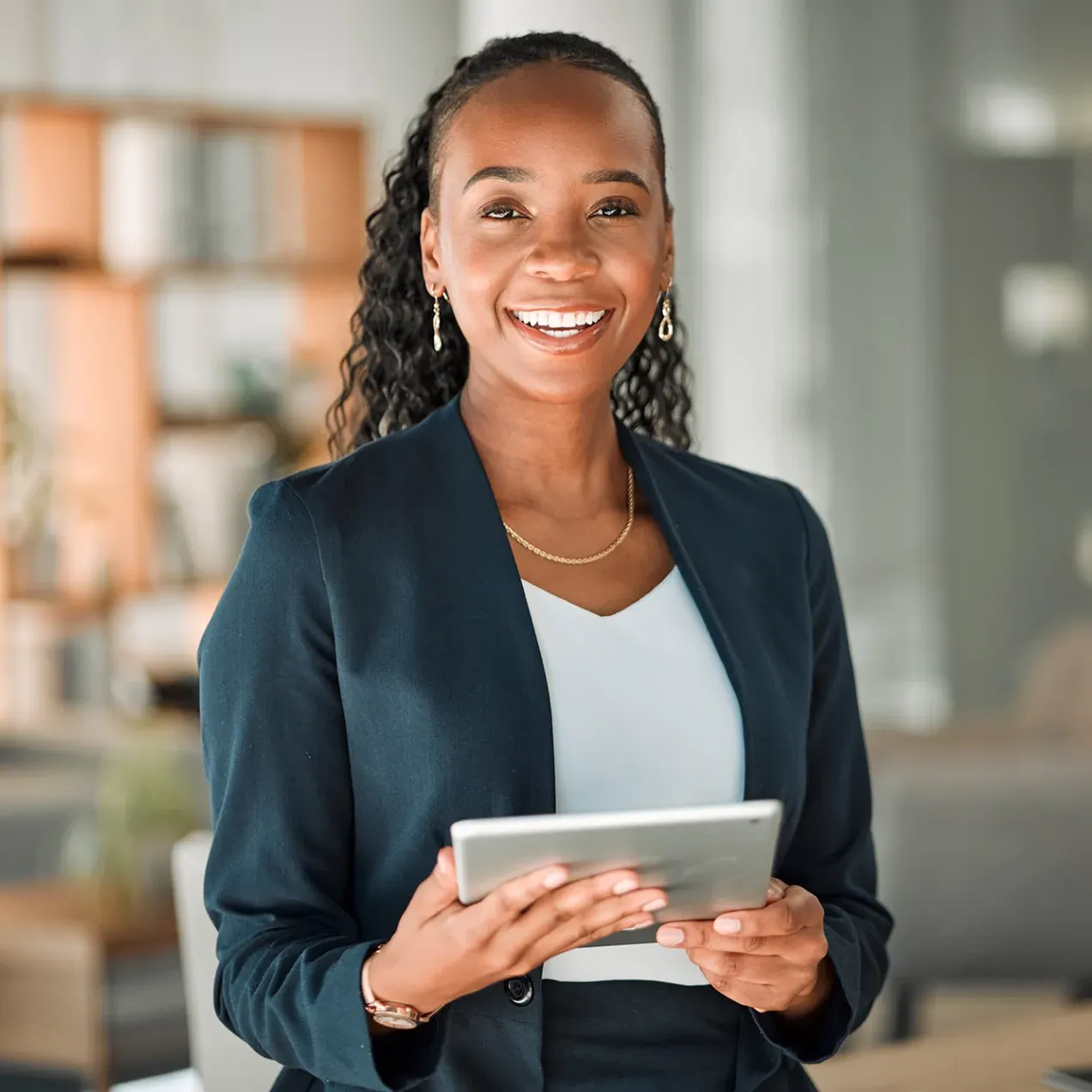 A smiling professional in business attire holds a tablet, representing career advancement opportunities with an MBA.